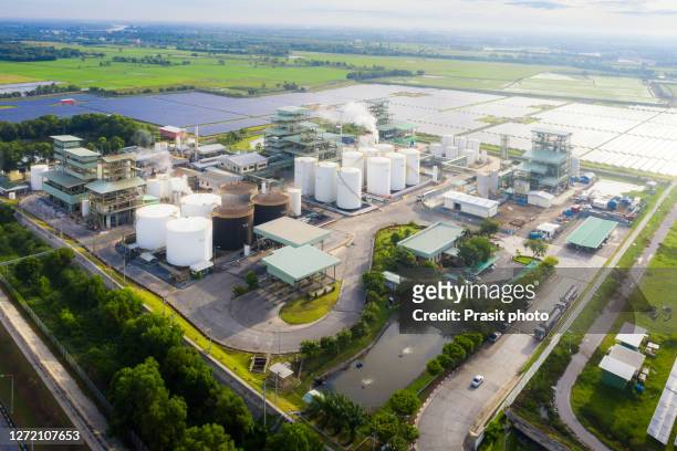 aerial view photo of industrial zone showing oil refinery with storage tank with solar farm power station for renewable energy supply. - herstellendes gewerbe stock-fotos und bilder