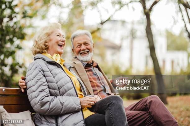 happy senior couple sitting on the bench in park - senior couple stock pictures, royalty-free photos & images