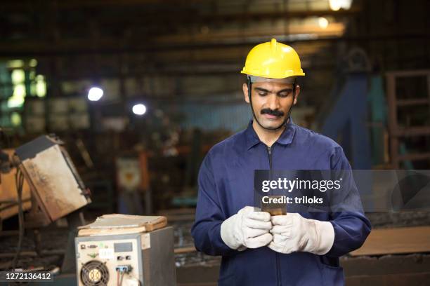 industrial worker in protective work wear texting on mobile phone at factory - india phone professional stock pictures, royalty-free photos & images