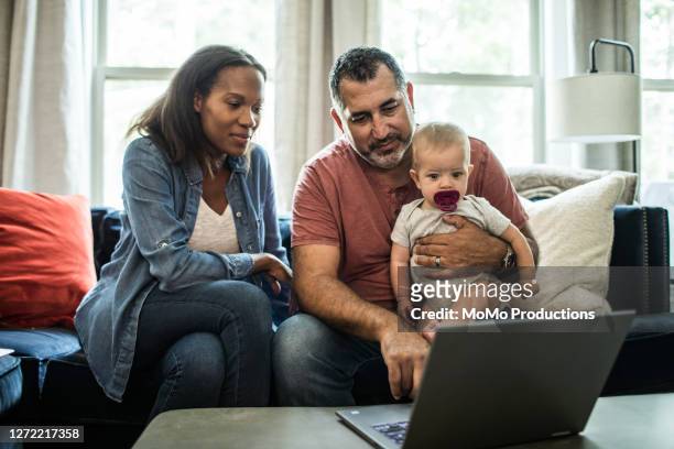 husband and wife holding baby and looking at laptop - two parents stock pictures, royalty-free photos & images