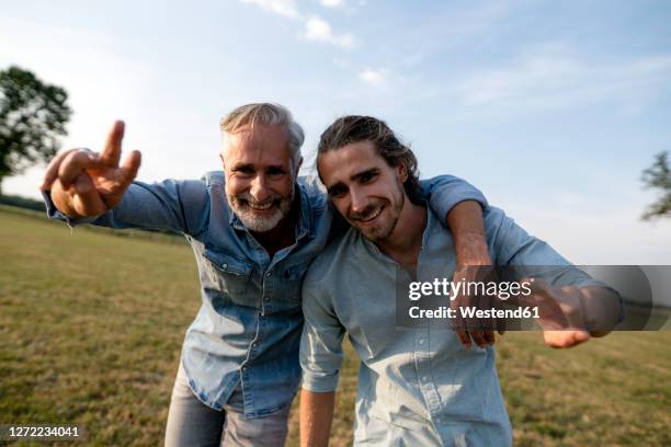 portrait of happy father with adult son on a meadow in the countryside - victory sign man stockfoto's en -beelden