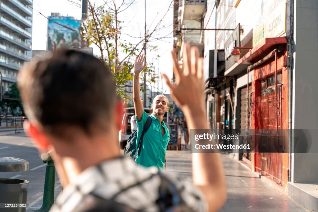 Gay couple waving hands at each other on sidewalk in city