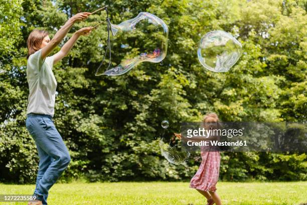 happy daughter exploding bubble with mother at park - bubbles happy stockfoto's en -beelden