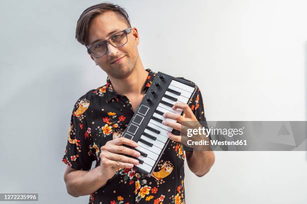 smiling man holding midi keyboard while standing against wall - keyboard instrument stock pictures, royalty-free photos & images