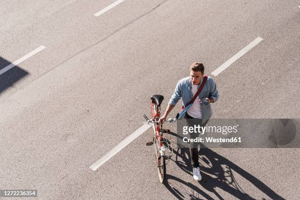 young man crossing street with bicycle in city - leben in der stadt stock-fotos und bilder