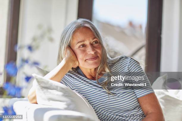 smiling woman relaxing on sofa in living room - cheveux gris photos et images de collection