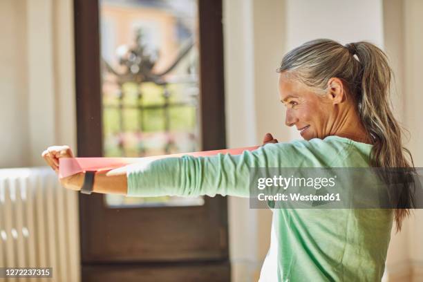 smiling woman exercising with resistance band in living room - hair woman mature grey hair beauty stock pictures, royalty-free photos & images