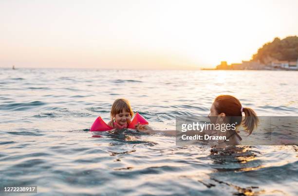 three year old girl swimming in the sea learning to swim, wearing water wings - mother and child in water at beach stock pictures, royalty-free photos & images