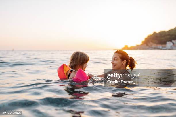 niña de tres años nadando en el mar aprendiendo a nadar, usando alas de agua - brazaletes acuáticos fotografías e imágenes de stock