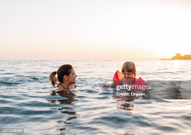 three year old girl swimming in the sea learning to swim, wearing water wings - mother and child in water at beach stock pictures, royalty-free photos & images