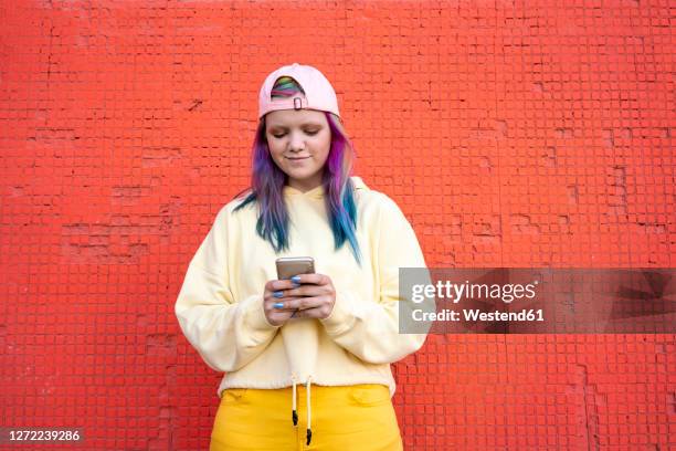 portrait of young woman with dyed hair using smartphone in front of yellow wall - dyed red hair fotografías e imágenes de stock