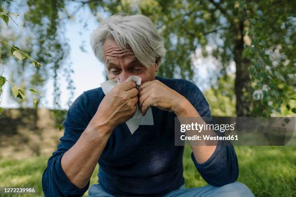 wrinkled man blowing nose while sitting in field - allergia foto e immagini stock