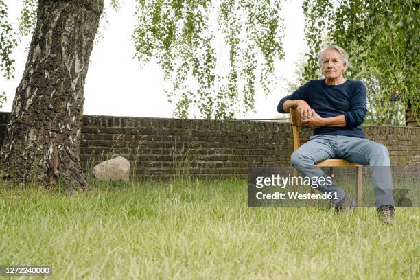 contemplating man sitting on chair against brick wall in backyard - sitzen stock-fotos und bilder