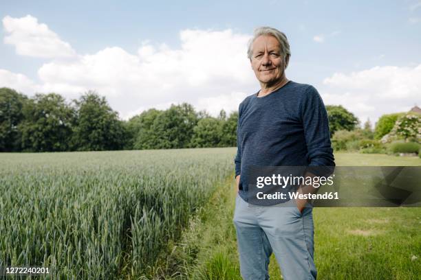 smiling man with hands in pockets standing in field - three quarter length photos stock pictures, royalty-free photos & images