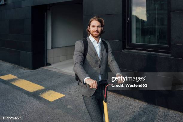 confident handsome male entrepreneur riding electric push scooter to commute in downtown - man on scooter stock pictures, royalty-free photos & images