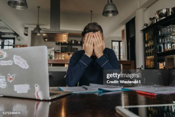 overstressed young man studying from home, covering face with his hands - homework frustration stock pictures, royalty-free photos & images