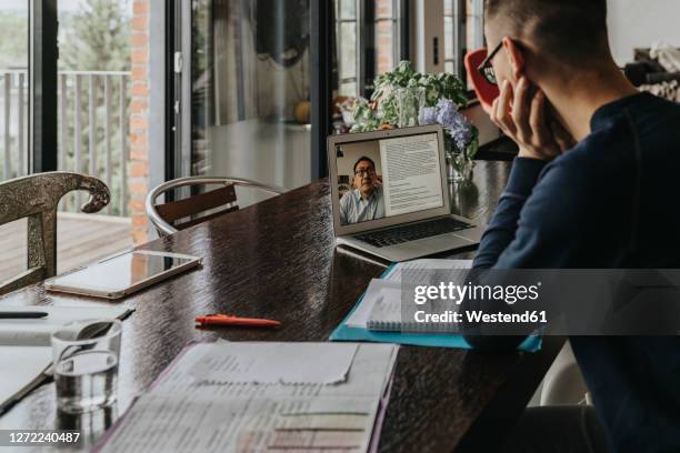 young man studying from home, using laptop - book on table foto e immagini stock