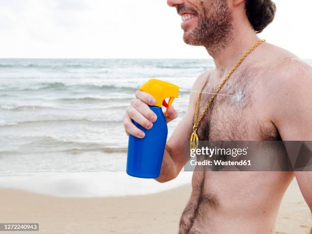 smiling man applying suncream at beach - torse velu photos et images de collection