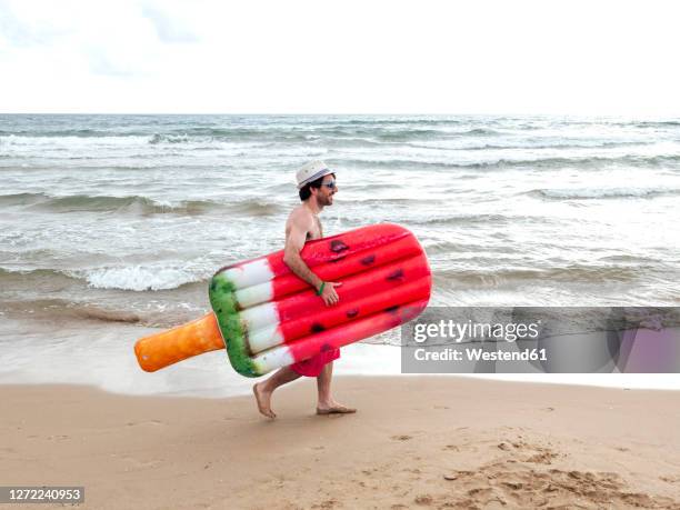 man walking with airbed on the beach - icecream beach stock pictures, royalty-free photos & images