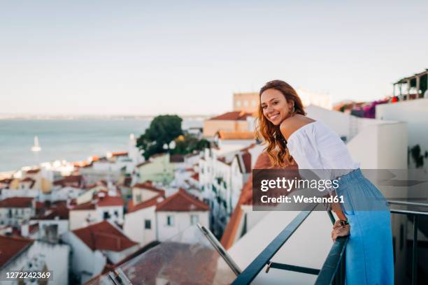 young woman smiling while standing at rooftop at alfama, lisbon, portugal - lisbon tourist stock pictures, royalty-free photos & images