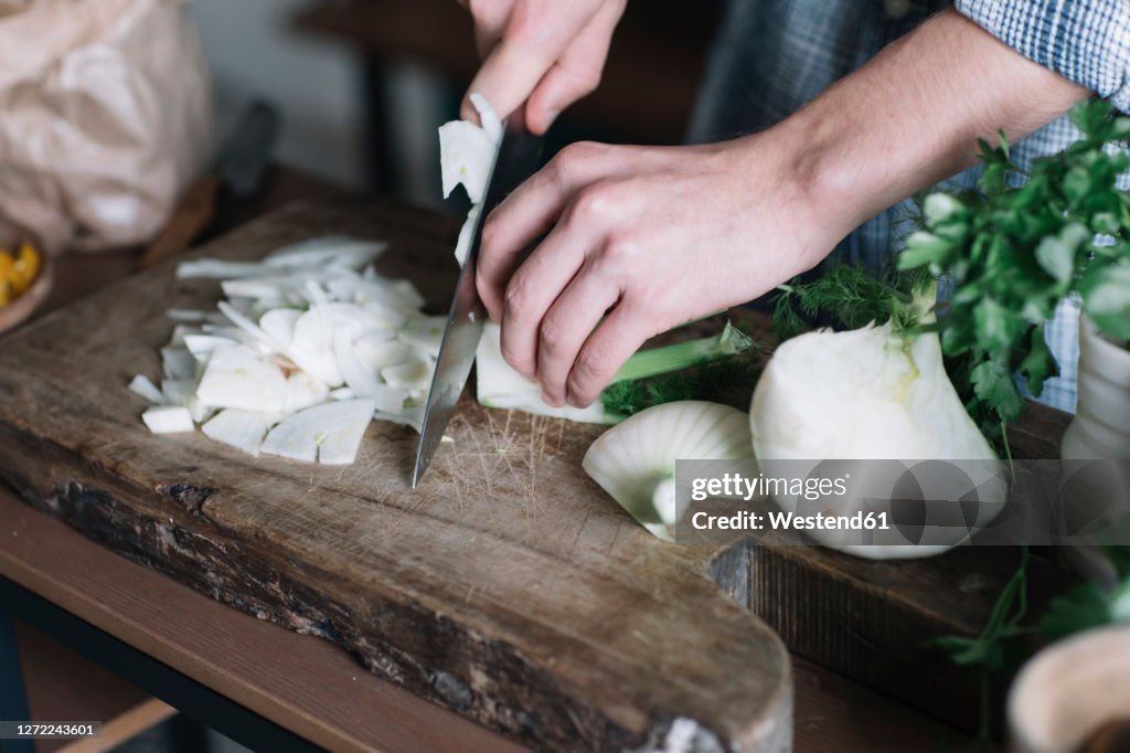 Hands of man cutting fennel on board in kitchen
