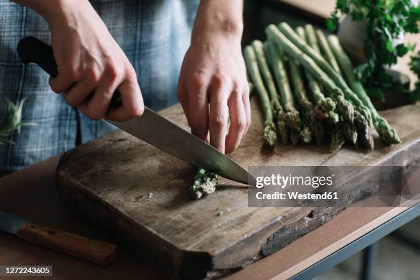 hands of man cutting fresh asparagus on board in kitchen - kitchen knife stockfoto's en -beelden