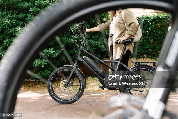 woman with electric bicycle seen through wheel - ebike stock-fotos und bilder