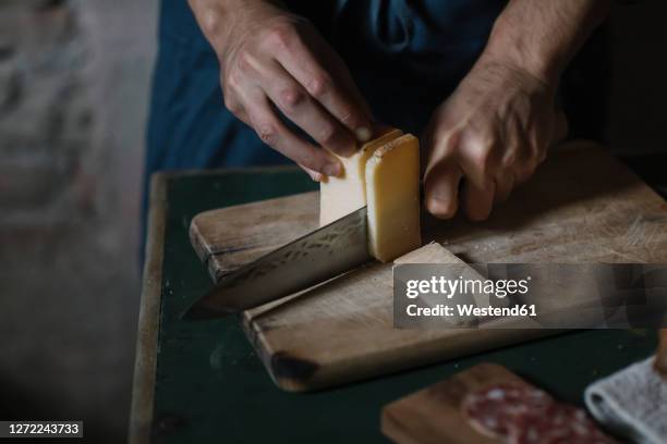 hands of man cutting artisanal cheese slices on board at table - fis photos et images de collection