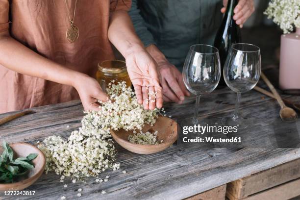 midsection of couple preparing fresh cocktail with white flowers on wooden table - cocktail making stock pictures, royalty-free photos & images