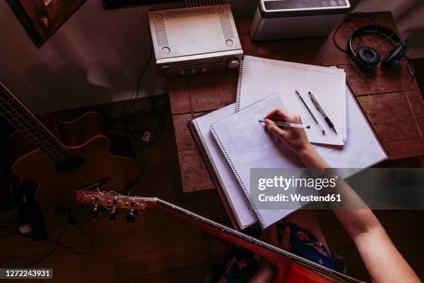 young woman writing in book while practicing guitar at home - liedermacher stock-fotos und bilder