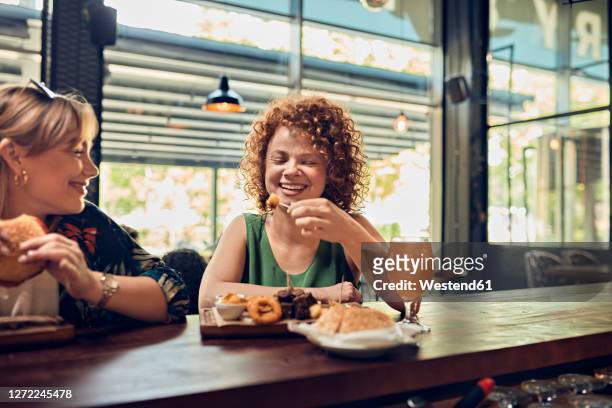 two happy female friends having a snack at the counter in a pub - tapas stock-fotos und bilder