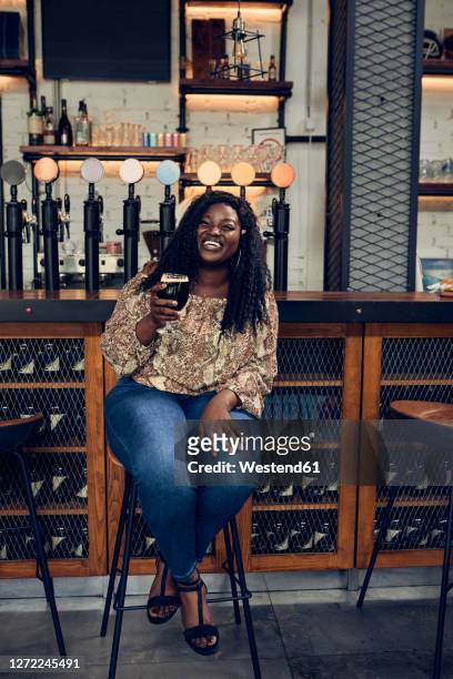 happy woman sitting at the counter in a pub having a beer - bar front stock-fotos und bilder