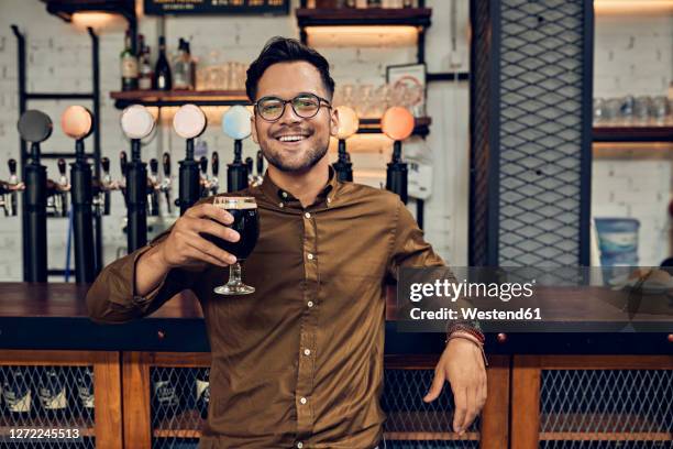 portrait of a smiling man raising his beer glass in a pub - man sipping beer smiling stockfoto's en -beelden
