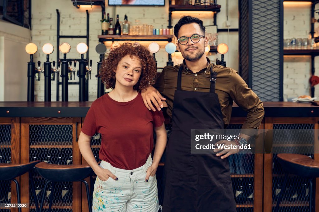 Portrait of confident owner couple at the counter in a pub