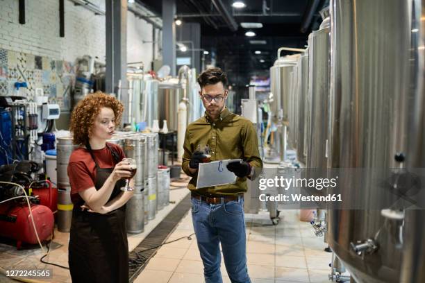 man and woman working in craft brewery discussing quality of a beer - clipboard and glasses stock pictures, royalty-free photos & images