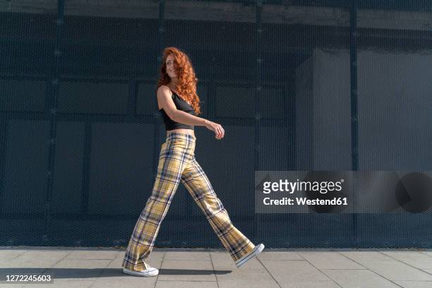 woman looking over shoulder while walking on sidewalk by fence - woman walking stock-fotos und bilder
