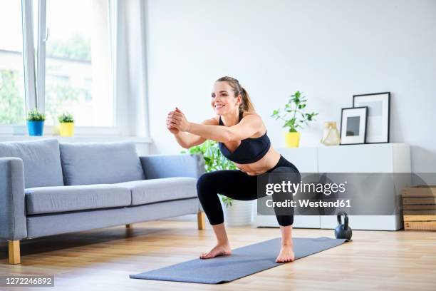 smiling woman doing squats during home workout - squatting position - fotografias e filmes do acervo