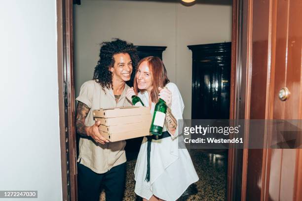 cheerful friends with beer bottle and pizza boxes at entrance of home during party - pizza box stock-fotos und bilder