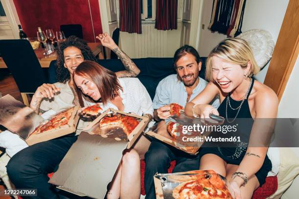 cheerful friends watching tv while eating pizza during party at home - celebrating in sofa stock pictures, royalty-free photos & images