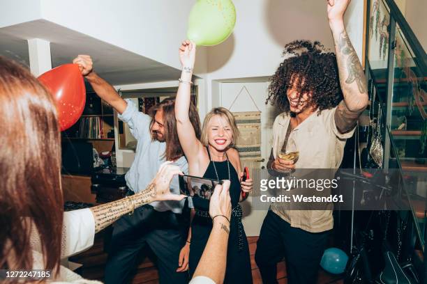 woman photographing happy friends dancing during social gathering at home - house after party stock pictures, royalty-free photos & images