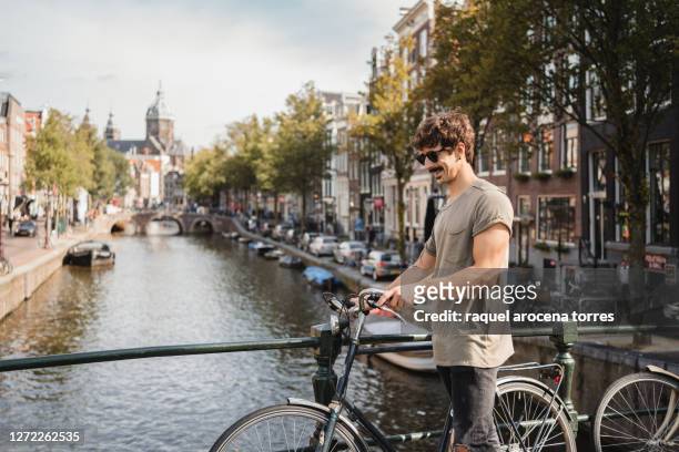 adult white man riding bikes in amsterdam - amsterdam canals stockfoto's en -beelden