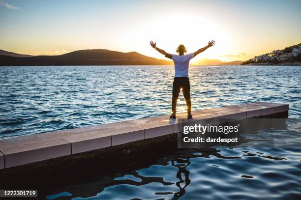 uomo maturo a braccia aperte al tramonto al mare - open workouts foto e immagini stock