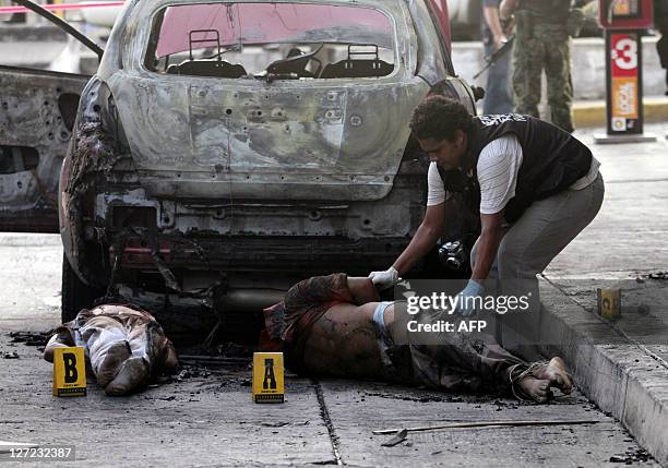 Police officer moves one of five corpses found with a burnt car in Acapulco, Guerrero state, Mexico on September 26, 2011. Seven people were killed...