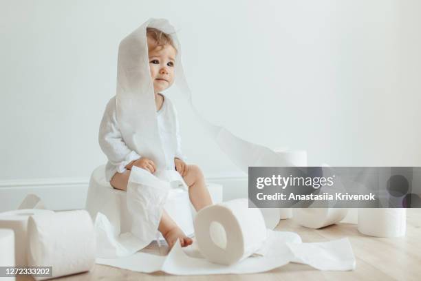 cute baby girl sitting on white chamber pot with toilet paper rolls. funny toddler sitting on potty chair and playing with toilet paper. - baby pee stockfoto's en -beelden