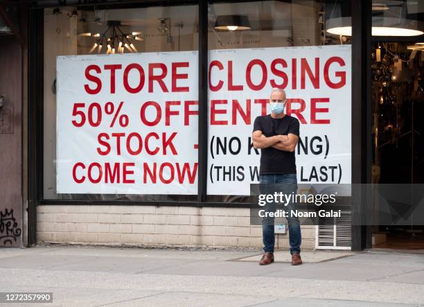 Person wearing a protective mask stands by a going out of business sign displayed outside a retail store as the city continues Phase 4 of re-opening...