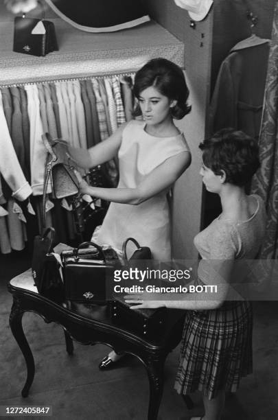 Portrait de Sheila montrant un sac à main à une cliente de la "boutique de Sheila", en novembre 1964.