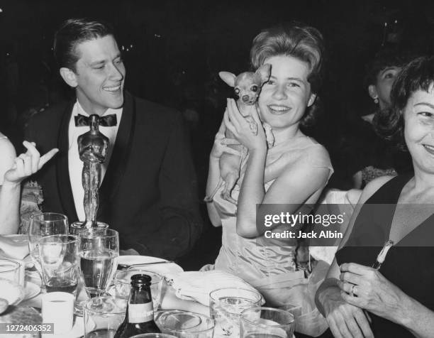 American actress Patty Duke holds her pet chihuahua, Bambi, while seated next to Andrew Prine during the Academy Awards party held at the Hilton...