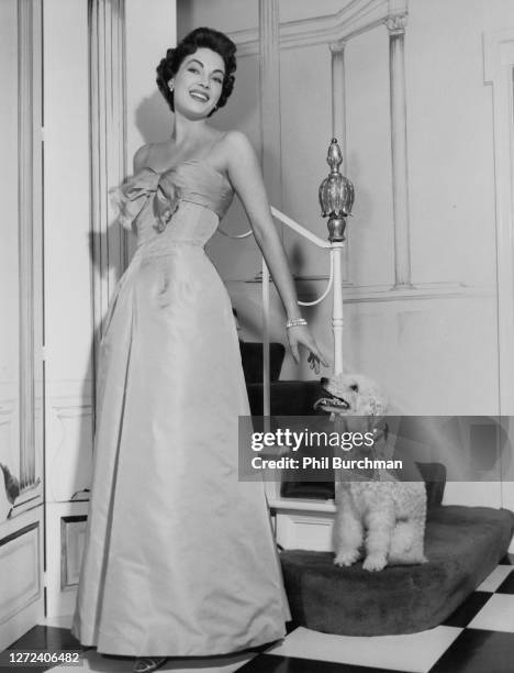 American actress Jarma Lewis , wearing pale silver grey evening gown with fringed bow band in taffeta by Amelia Gray, stands next to a staircase with...