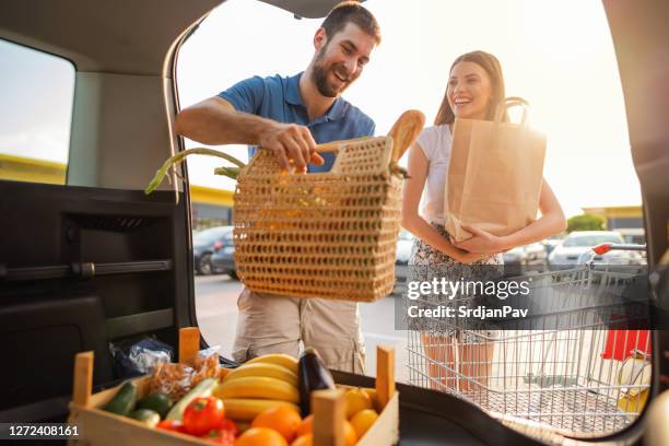 glückliches paar packt lebensmittel aus supermarkt in kofferraum - couple in supermarket stock-fotos und bilder