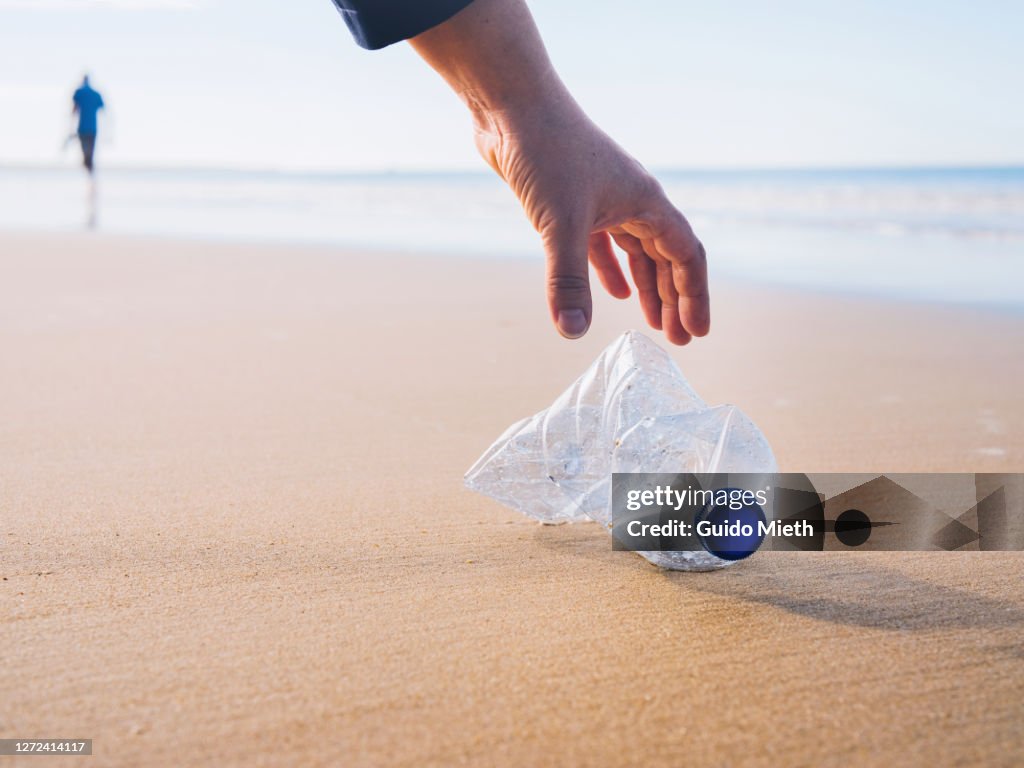 Hand picking up plastic bottle at beach.